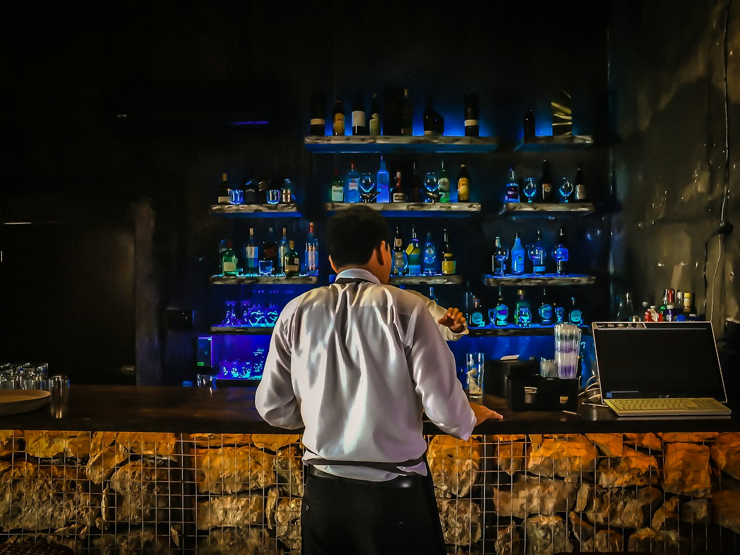 Barkeeper mixt Getränke hinter einer beleuchteten Bartheke.